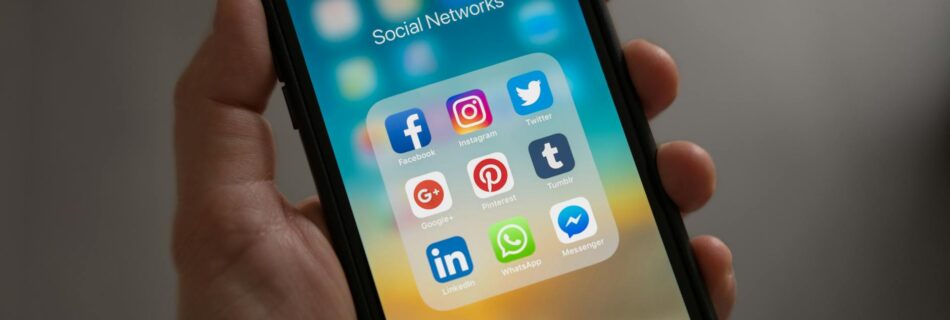 person holding iphone showing social networks folder